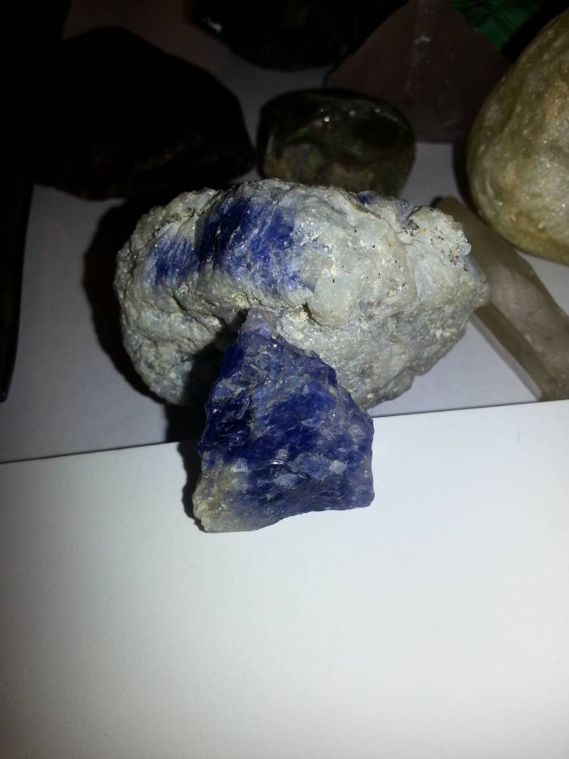 Blue violet rough stone displayed beside mineral-bearing matrix