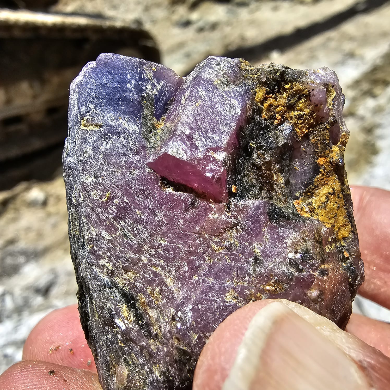Close view of a purple red rough gemstone in matrix